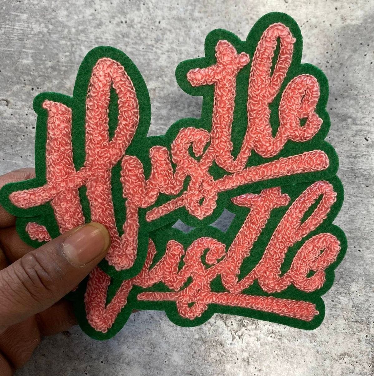 Red and green fuzzy script chenille patch with the word Hustle Hustle, great for varsity and streetwear jackets.