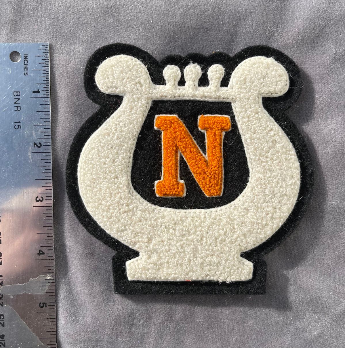 White chenille patch outlined in black with orange letter N, available as iron-on or sew-on backing for varsity jackets.
