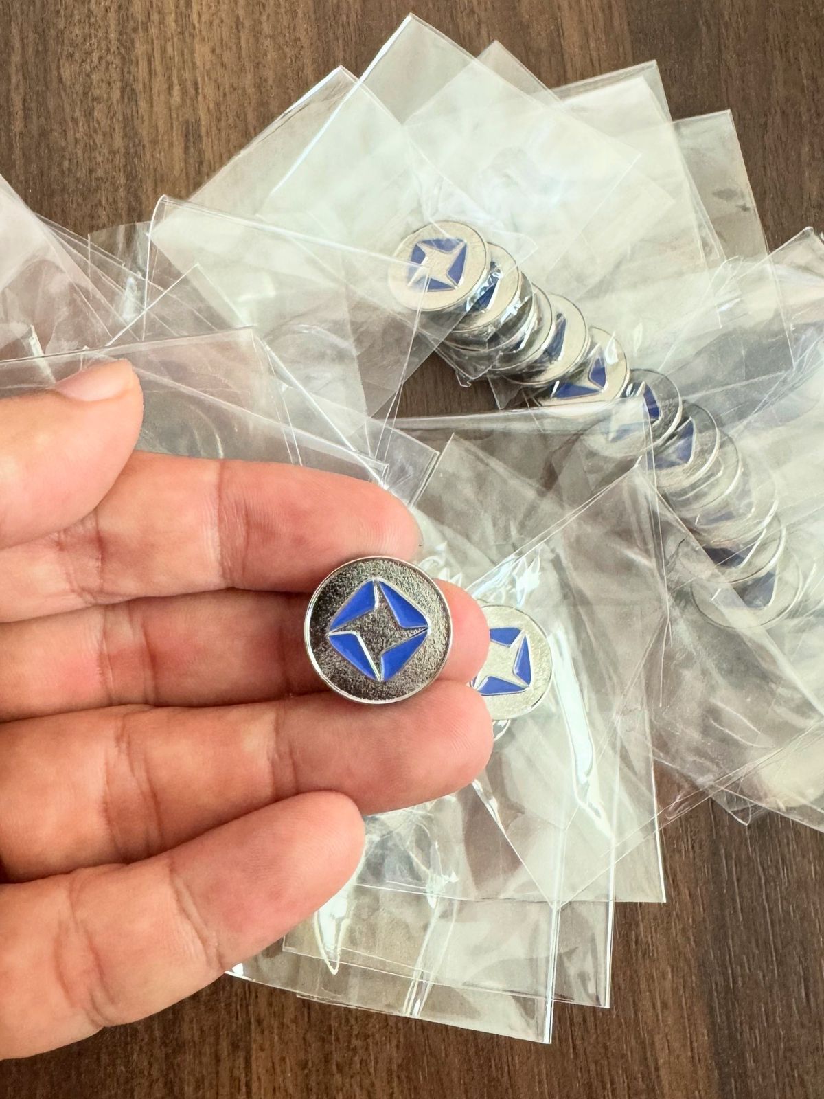 Hand holding a custom blue star enamel lapel pin with silver finish and butterfly clutch backing, bulk branded custom pin badges for corporate and organizational use.